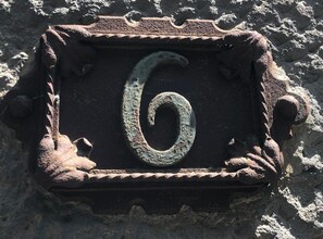 Un letrero metálico desgastado con el número 6, fijado en una pared con textura.