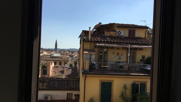 A view from a window overlooking a cityscape with traditional architecture, including terracotta-tiled roofs and a prominent tower in the distance. - Fortezza Fourth Floor - 6 pax (Florence)