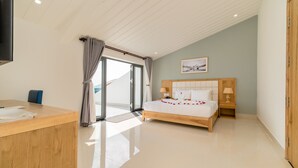 A modern hotel room with a wooden desk, a bed with white linens, a wooden headboard, two bedside tables with lamps, and a large window with curtains. - Babylon Hoi An Central Villa (Da Nang)
