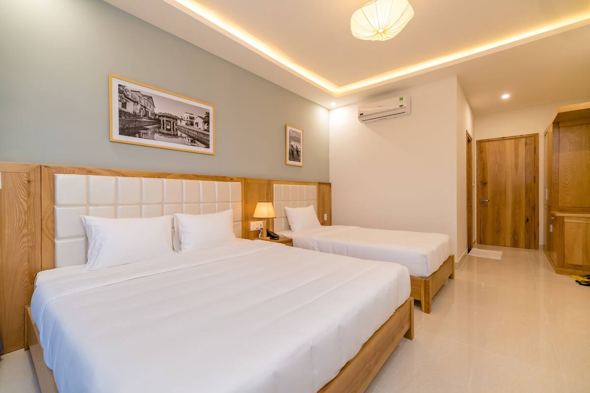 A hotel room with two beds, a wooden headboard, a nightstand, a lamp, and a framed picture on the wall.