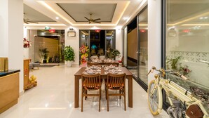 A dining area with a long table set for six, surrounded by wooden chairs. There is a ceiling fan above the table, and the room has a modern design with a glass partition on one side. - Babylon Hoi An Central Villa (Da Nang)