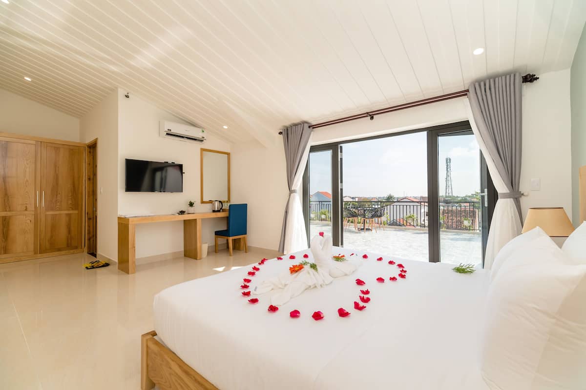 A hotel room with a large bed, a desk, a TV, and a balcony with a view of the city.