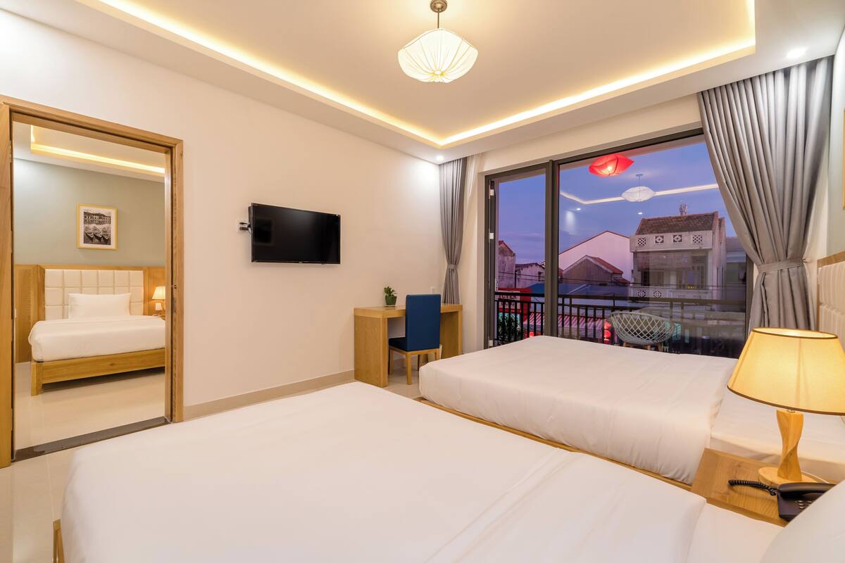 A hotel room with two beds, a desk, a chair, a TV, and a window with a view of buildings.