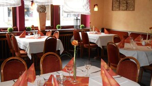 A restaurant with multiple tables set for dining, each with a white tablecloth, orange napkins, and wine glasses. - Hotel Niederée (Bad Breisig)