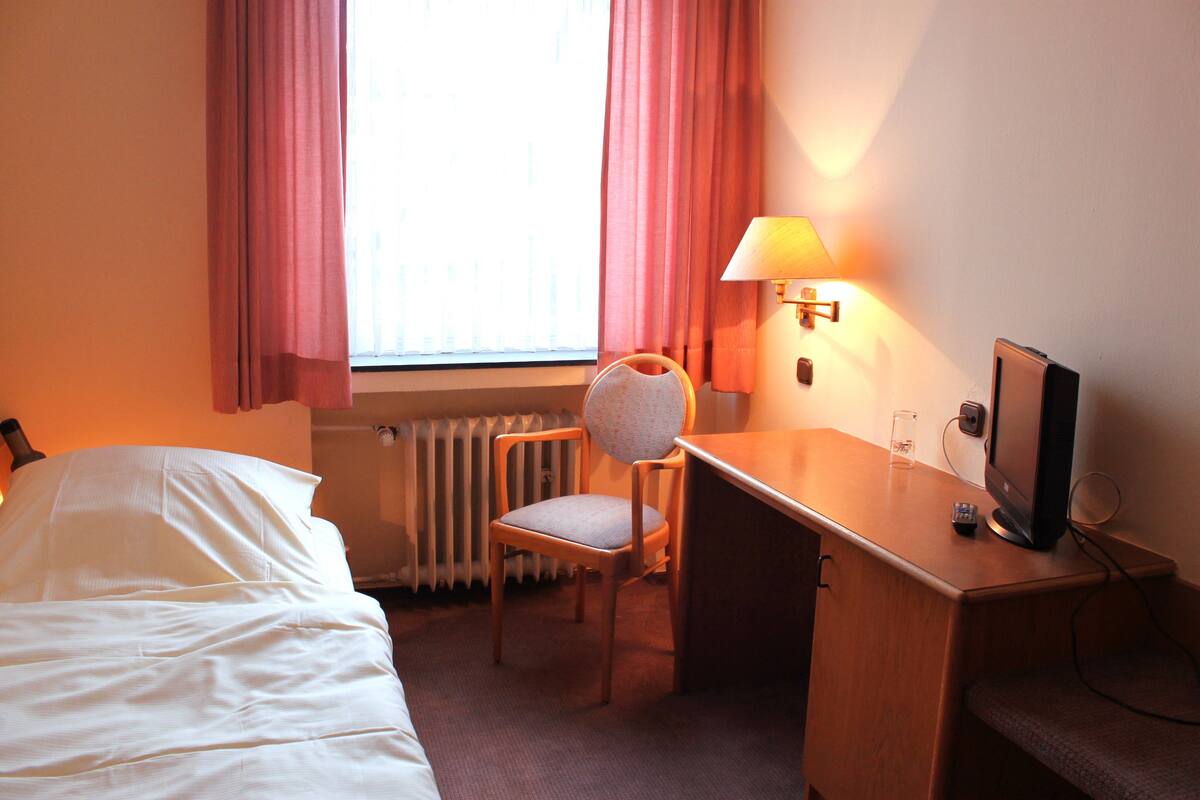 A hotel room with a bed, a desk with a chair, a television, and a lamp.