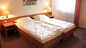 A double bed with white linens, two bedside tables with lamps, a painting on the wall, and a window with sheer curtains. - Hotel Niederée (Bad Breisig)