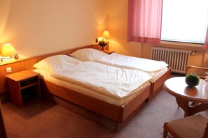 A double bed with a wooden frame, two bedside tables with lamps, a small round table with a plant, and a radiator. - Hotel Niederée (Bad Breisig)