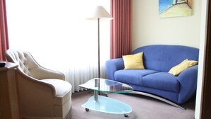 A living room with a blue sofa, a beige armchair, and a glass coffee table. - Hotel Niederée (Bad Breisig)