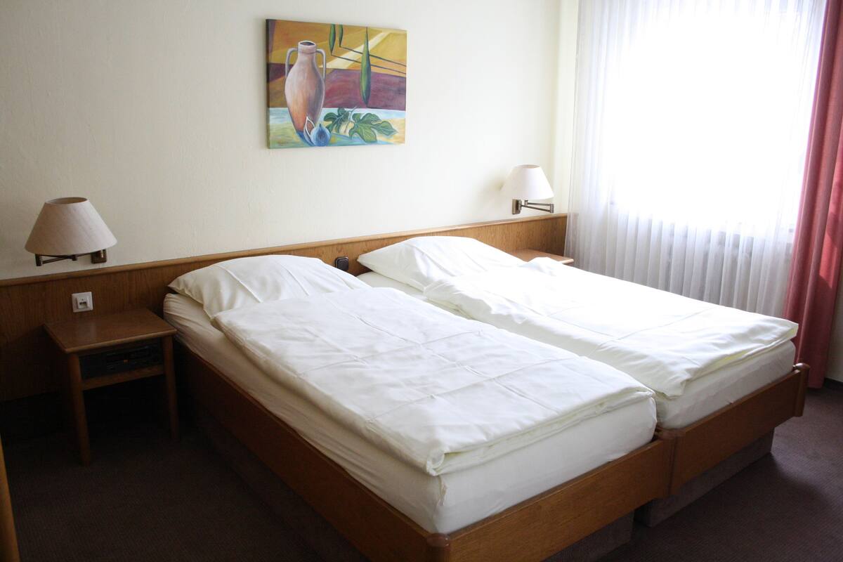 A hotel room with two beds, a nightstand, a lamp, and a painting on the wall.