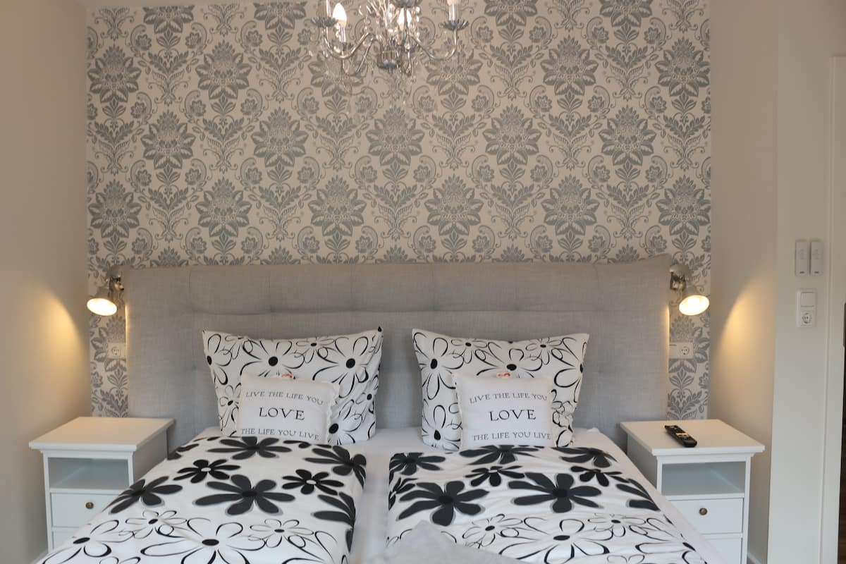A bedroom with a floral-patterned headboard, two bedside tables with lamps, and a bed with black and white floral bedding.