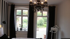 Un dormitorio con una cama grande, una ventana con cortinas, un candelabro y una mesita de noche.