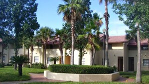 A building with a red-tiled roof, surrounded by palm trees and well-maintained grass. - Cozy One Bedroom Lakefront Villa Close to the Attractions (Orlando)
