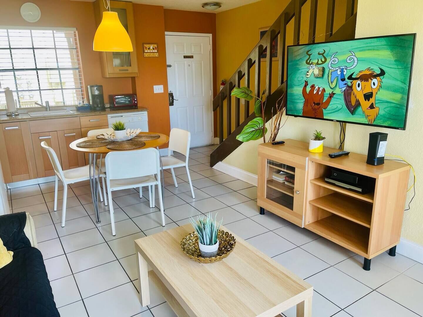 A modern living room with a dining area, a staircase, and a kitchen.