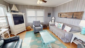A living room with a television, a grey armchair, a sofa, a coffee table, and a wooden wall decoration. - Ocean Front at the Washout~ Foose's Folly (Folly Beach)