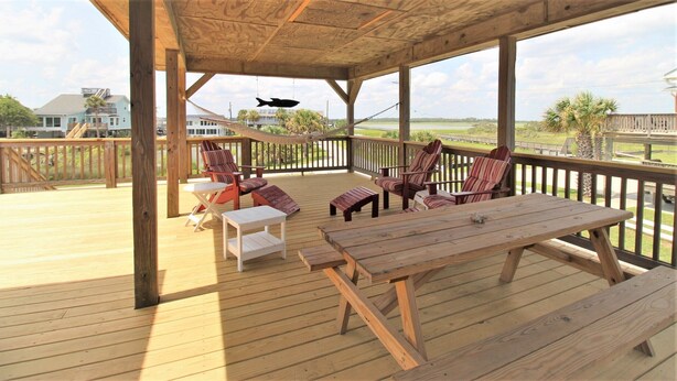 A wooden deck with outdoor furniture, including chairs and a table, overlooking a body of water and a residential area. - Ocean Front at the Washout~ Foose's Folly (Folly Beach)