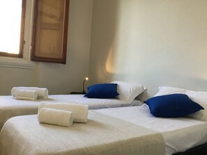 A hotel room with two beds, each with white linens and blue pillows. There are towels on the beds and a nightstand with a lamp. - Fortezza Fourth Floor - 4 pax (Florence)