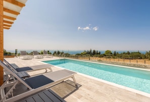 A poolside area with lounge chairs and a view of the sea. - Alonaki Apartments (Zakynthos)