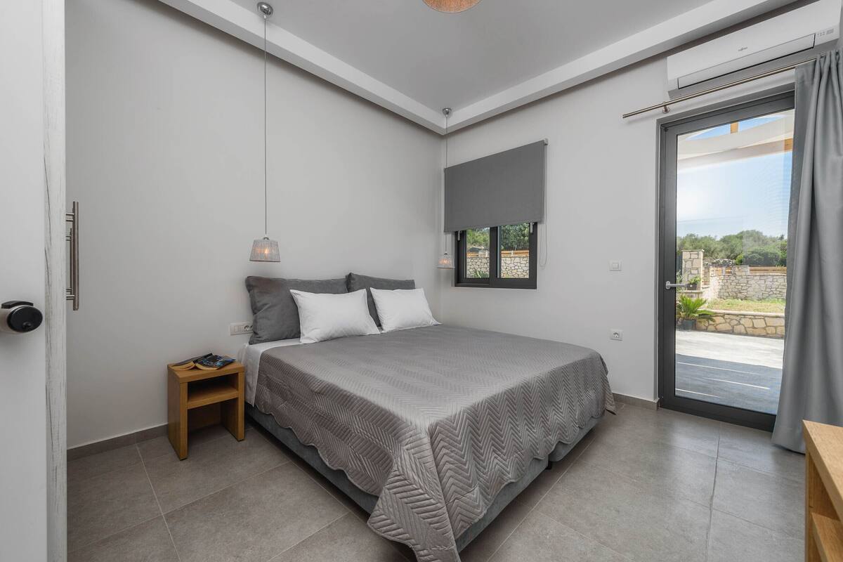 A bedroom with a bed, a nightstand, a window with a view, and a ceiling fan.