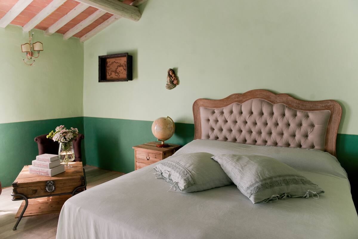 Une chambre à coucher bien rangée, avec un grand lit, une table de chevet en bois, un globe terrestre et un tableau encadré accroché au mur.