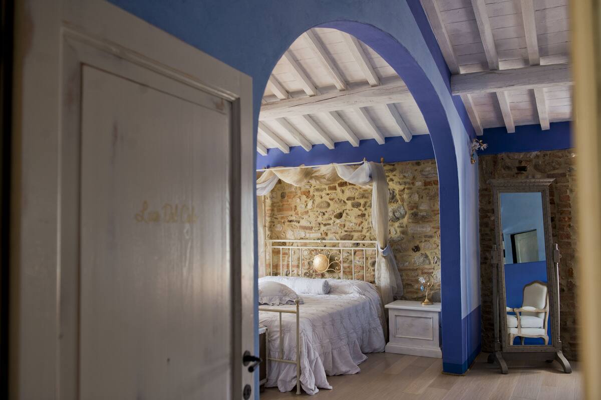 Une chambre avec un mur en pierre, un lit avec une literie blanche, une table de chevet et un miroir.