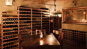 Une cave à vin avec des étagères en bois remplies de bouteilles, une table avec des chaises et des luminaires suspendus.