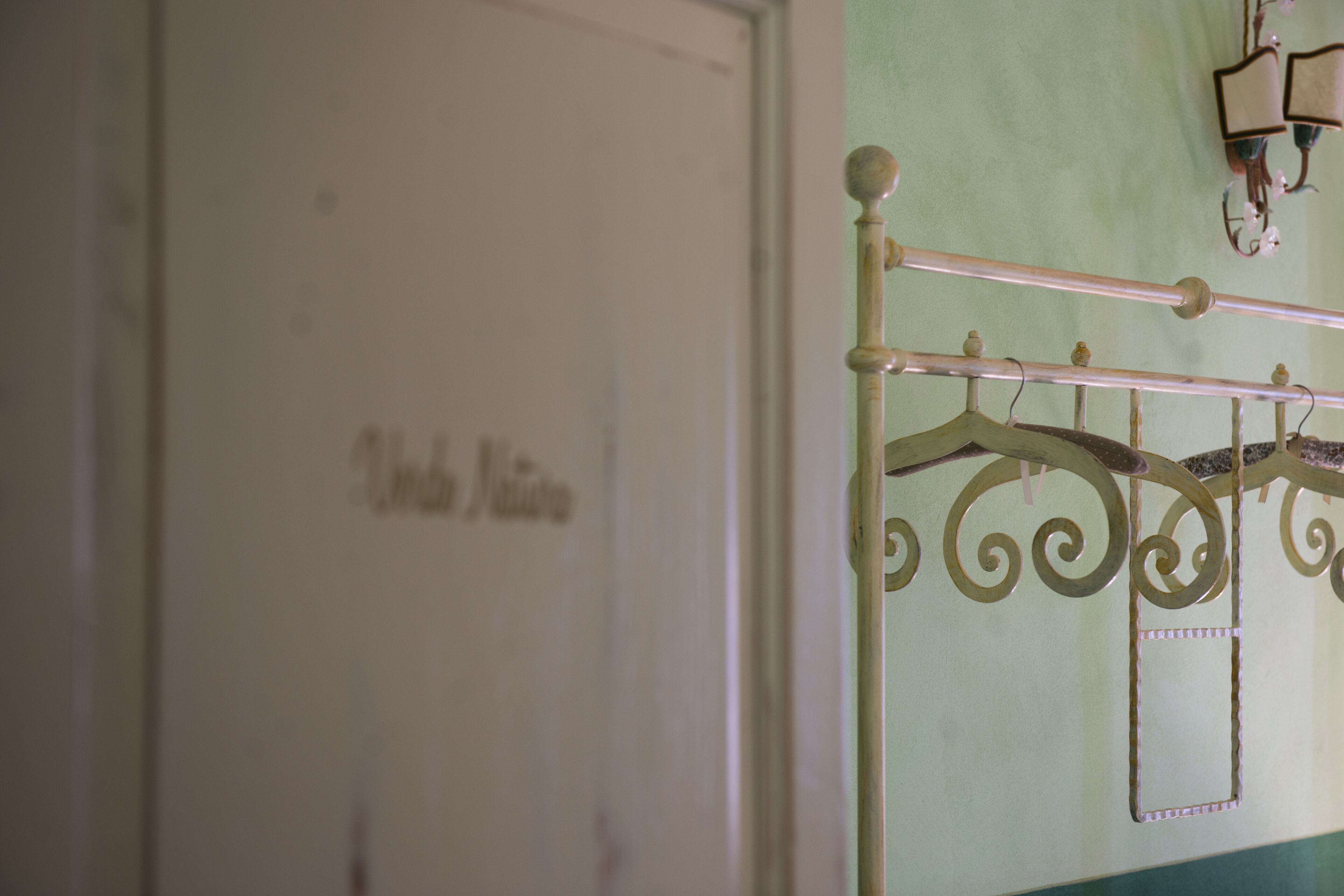 A white door with a nameplate, a metal bed frame with a decorative headboard, and a wall-mounted light fixture.