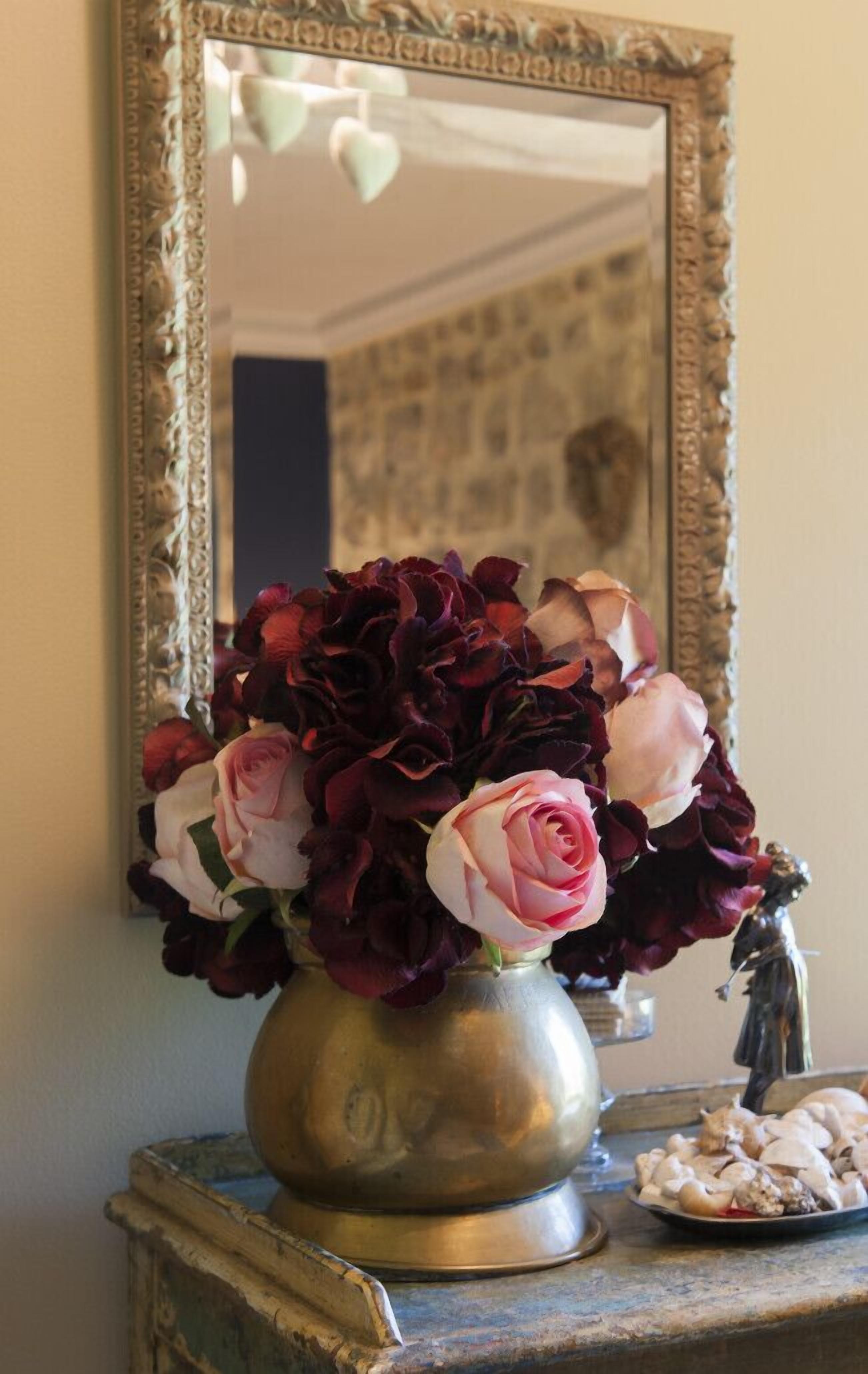 A vase with flowers on a table next to a mirror.