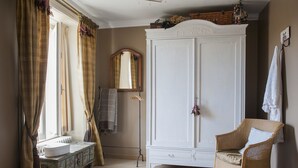 A room with a white wardrobe, a wicker chair, a radiator, and a mirror on the wall. - Chateau Le Colombier - Chambres d'hôtes (Carentan les Marais)