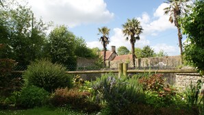 A stone building with a red roof, surrounded by lush greenery and palm trees. - Chateau Le Colombier - Chambres d'hôtes (Carentan les Marais)