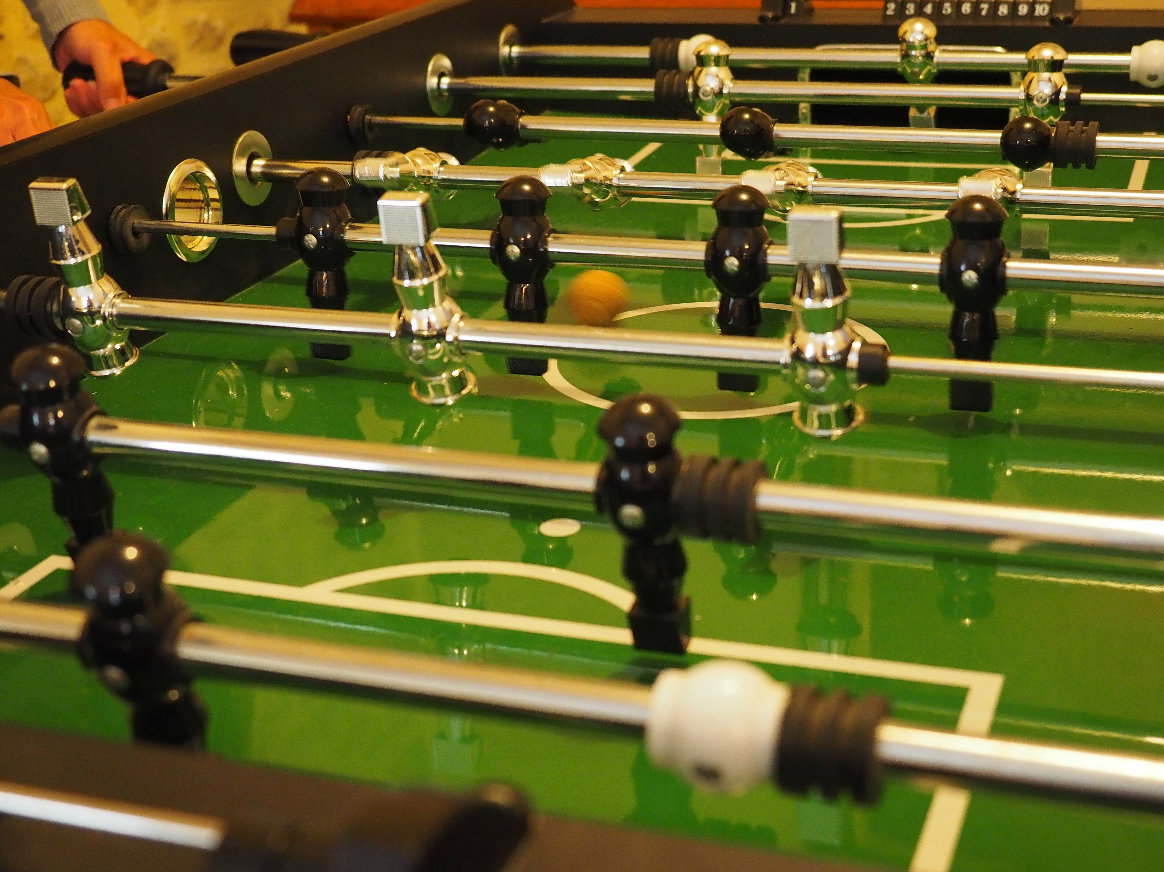 Un gros plan d’un baby-foot avec des barres et des joueurs noirs et argentés, et une surface de jeu verte.
