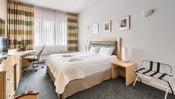 Et hotelværelse med seng, skrivebord, stol og et lille bord med lampe.