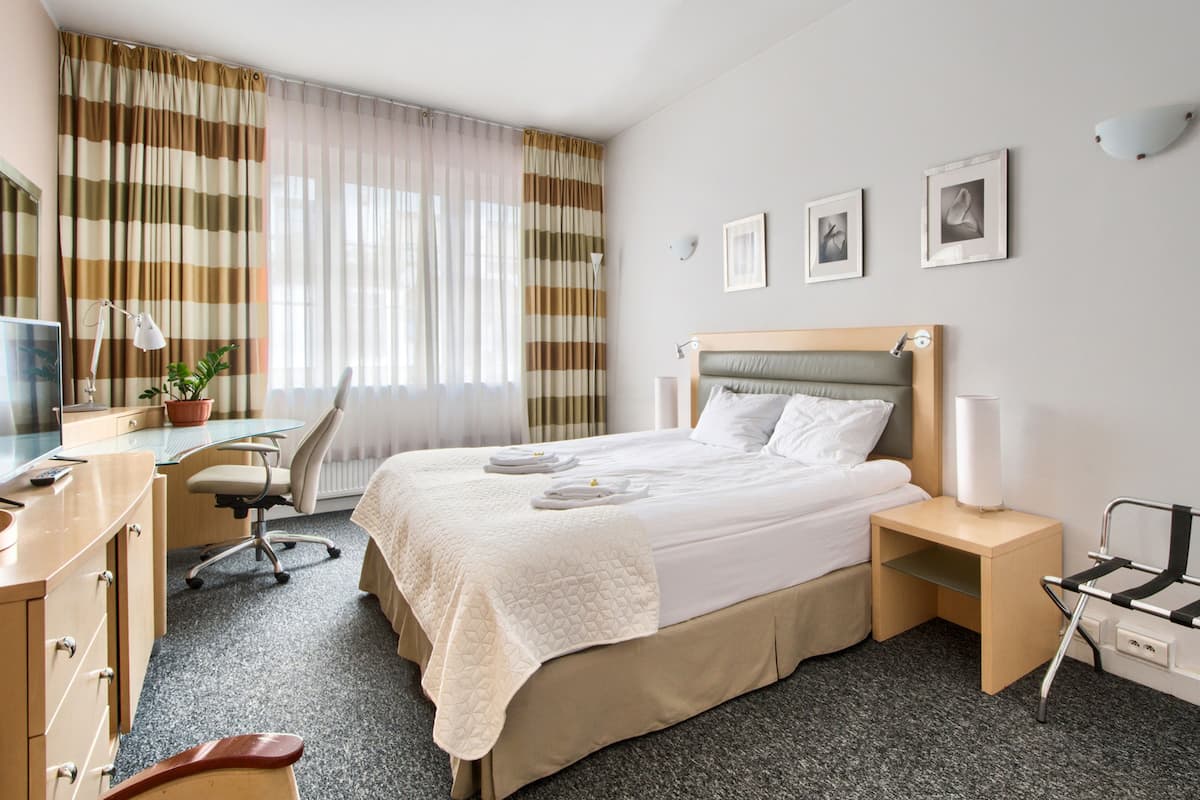 Een hotelkamer met een bed, bureau, stoel en een kleine tafel met een lamp.