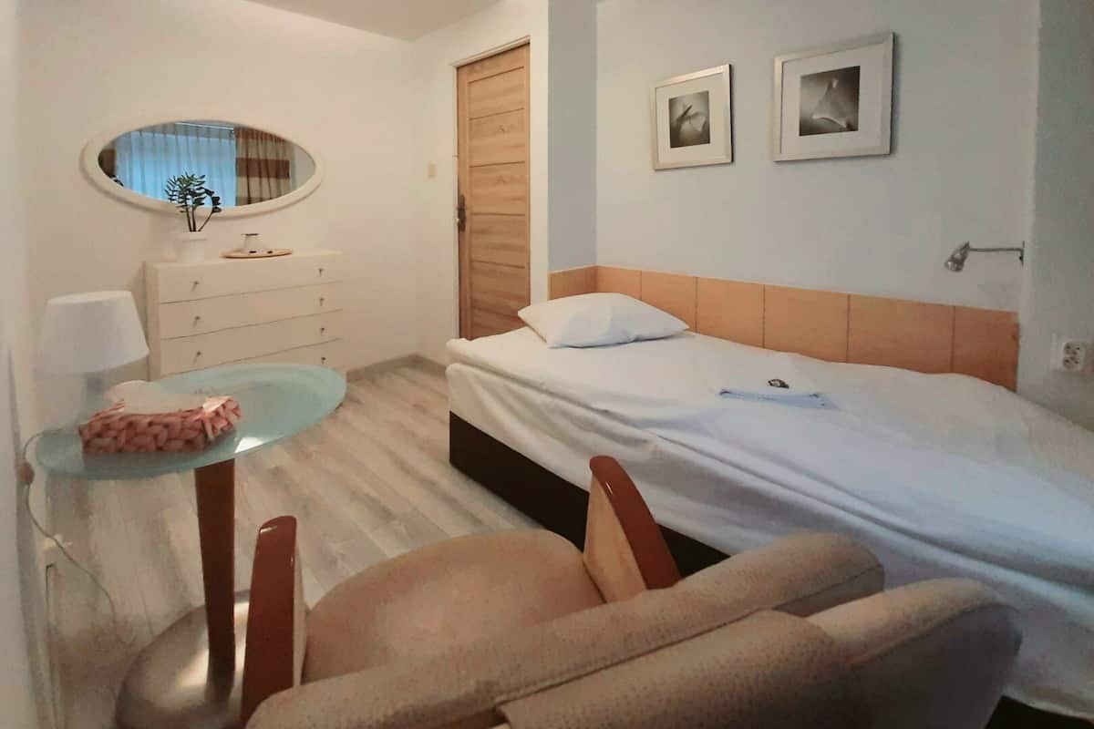 Een hotelkamer met een bed, een bureau met stoel, een spiegel en twee foto's in lijsten aan de muur.