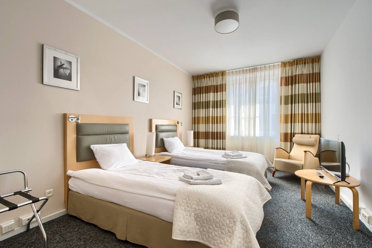 Een hotelkamer met twee bedden, een stoel, een televisie en een raam met gordijnen.