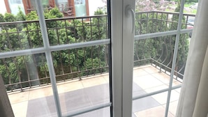 En balkon med gelænder i metal, udsigt til træer og en bygning i baggrunden.