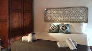 Un dormitorio con un armario de madera, una cama con cabecera estampada y dos almohadas con diseños geométricos.