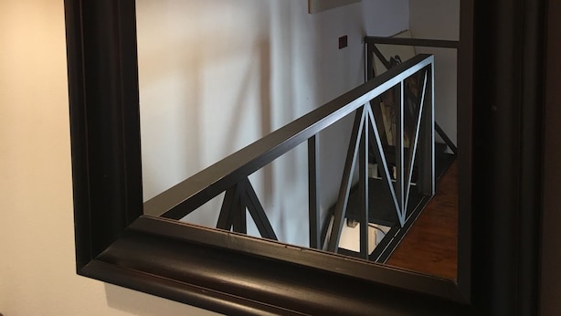Un espejo refleja una escalera con barandilla de metal negro y tres lámparas colgantes.
