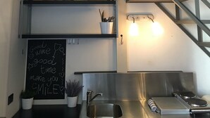 Una cocina con un lavamanos de acero inoxidable, una pizarra con un mensaje y un cuadro sobre la encimera.