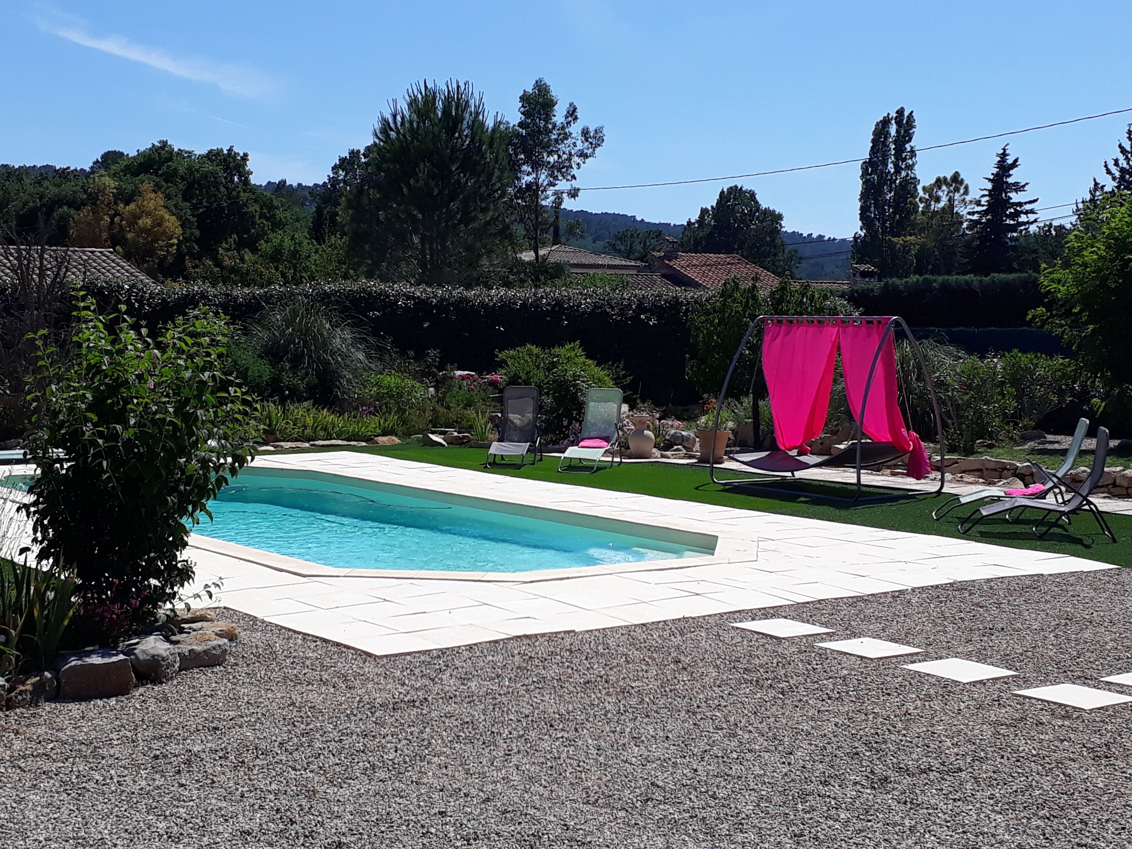 Ein Pool mit gefliestem Deck, umgeben von Grünpflanzen und einigen Liegestühlen.