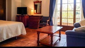A hotel room with a bed, a wooden table, a TV, a dresser, and a balcony with curtains. - Hotel Rural Castúo (Pinofranqueado)