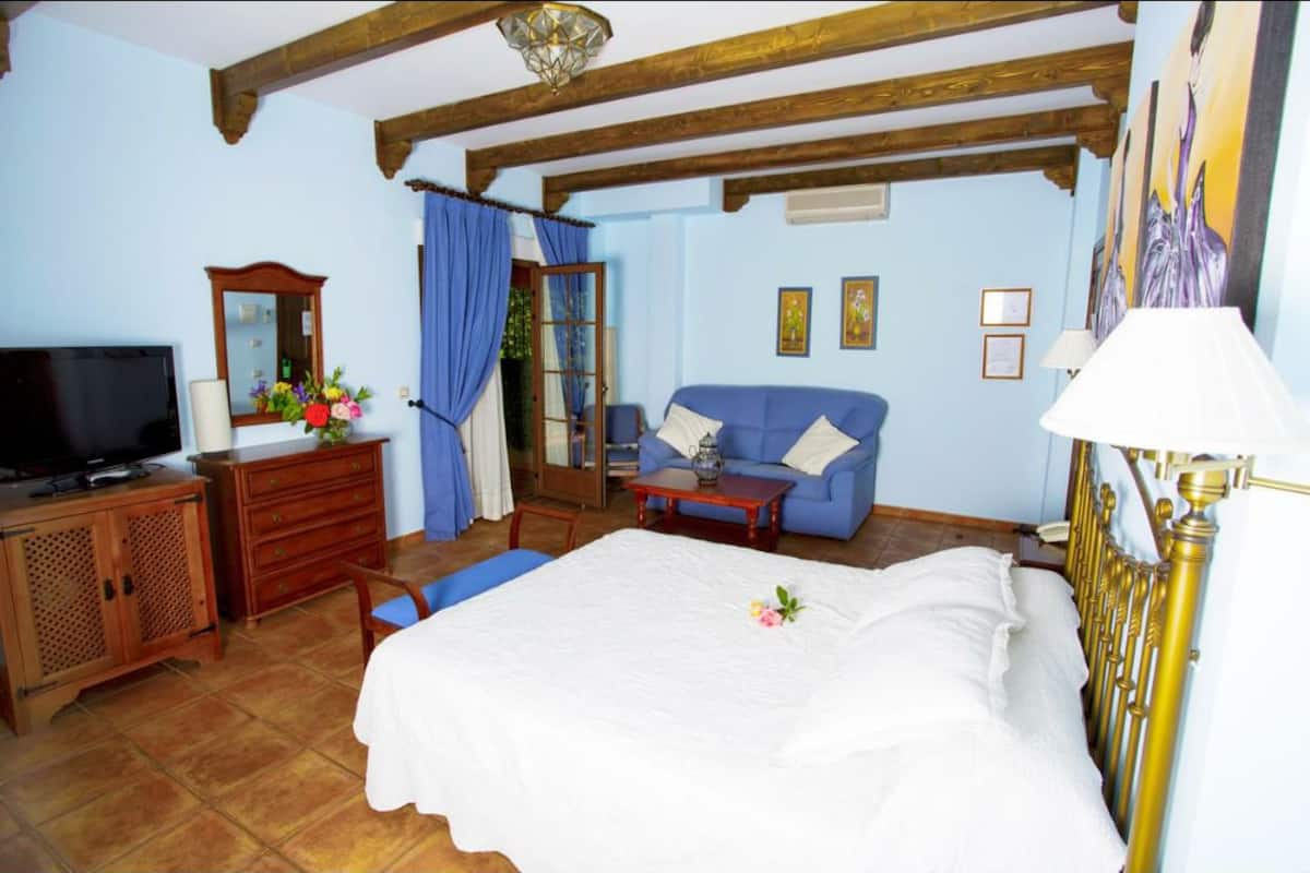 A bedroom with a bed, a television, a dresser, and a window with curtains.