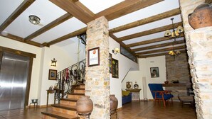 A spacious living area with a high ceiling and exposed wooden beams, stone pillars, and a staircase leading to an upper level. - Hotel Rural Castúo (Pinofranqueado)