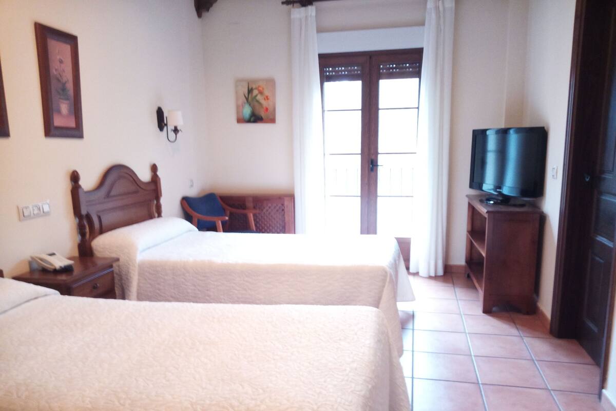 A hotel room with two beds, a television on a stand, a chair, and a door with a window.