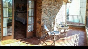 A room with a stone wall, a bed, and a balcony with wicker furniture. - Hotel Rural Castúo (Pinofranqueado)