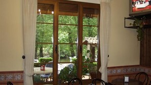 A dining area with a large window, wooden furniture, and a television on the wall. - Hotel Rural Castúo (Pinofranqueado)