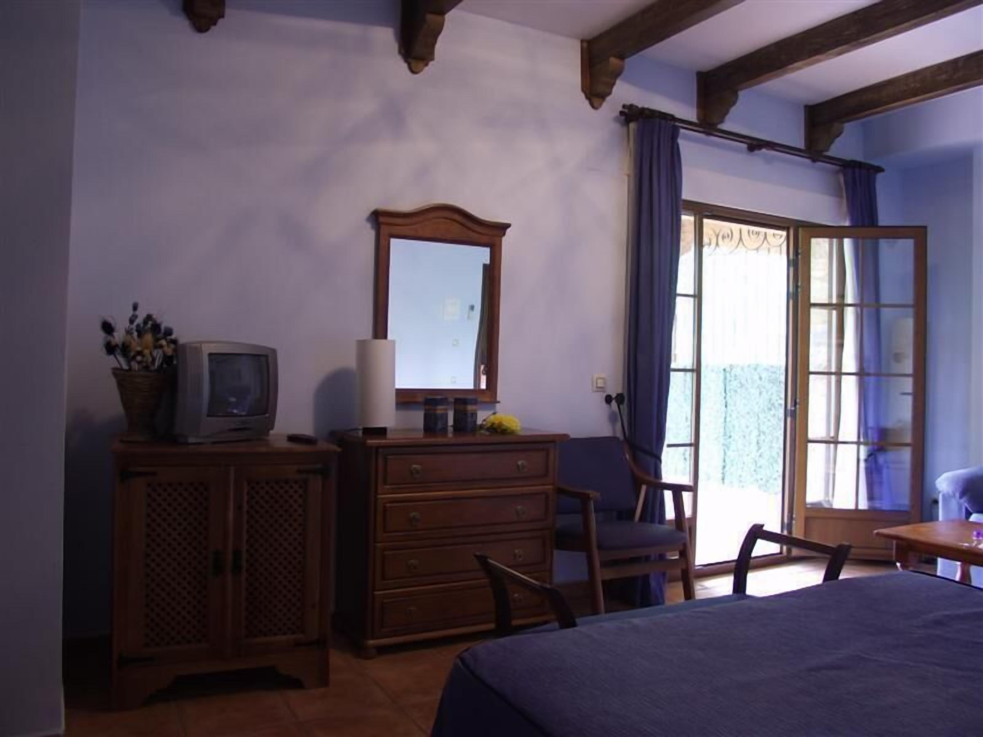 Una habitación con una cama, un aparador de madera, un televisor, un espejo y una ventana con cortinas.