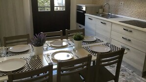 Un comedor con una mesa dispuesta para cuatro personas, rodeada de sillas de madera. Se observa una ventana con vistas a zonas verdes.