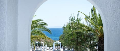 Vista a través de un arco de una zona de piscina con sillones de descanso y un pabellón, con vista al mar.