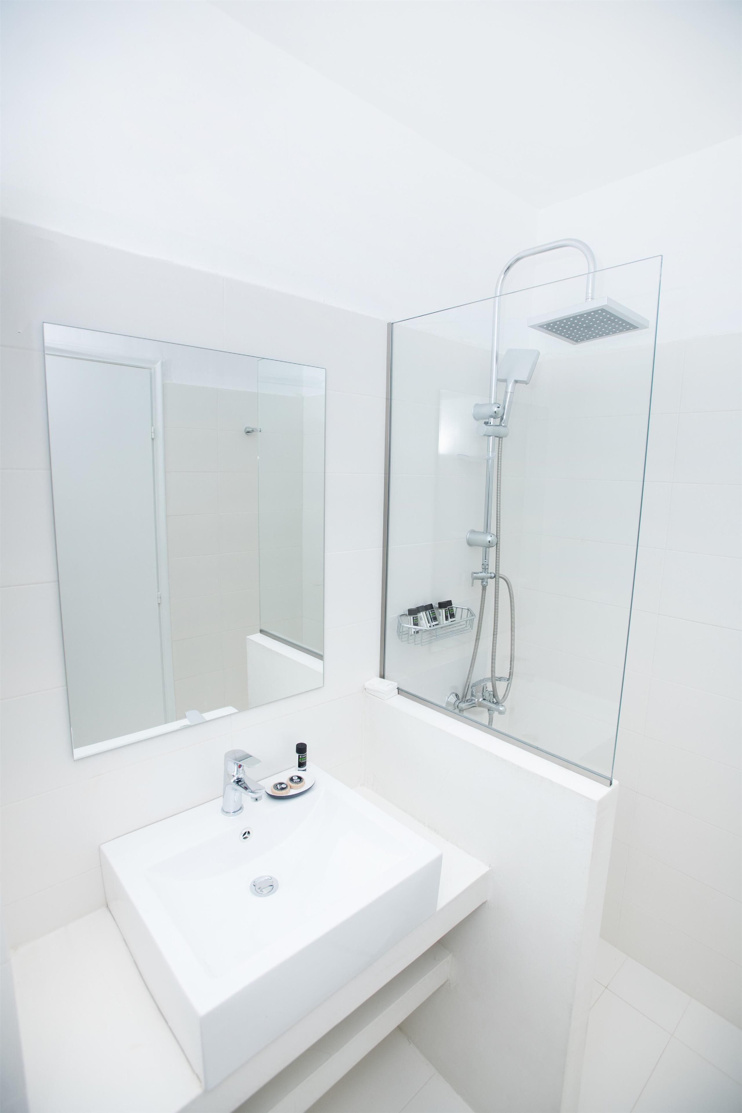 Un baño moderno con un lavamanos blanco, un espejo grande y una ducha con cerramiento de vidrio.