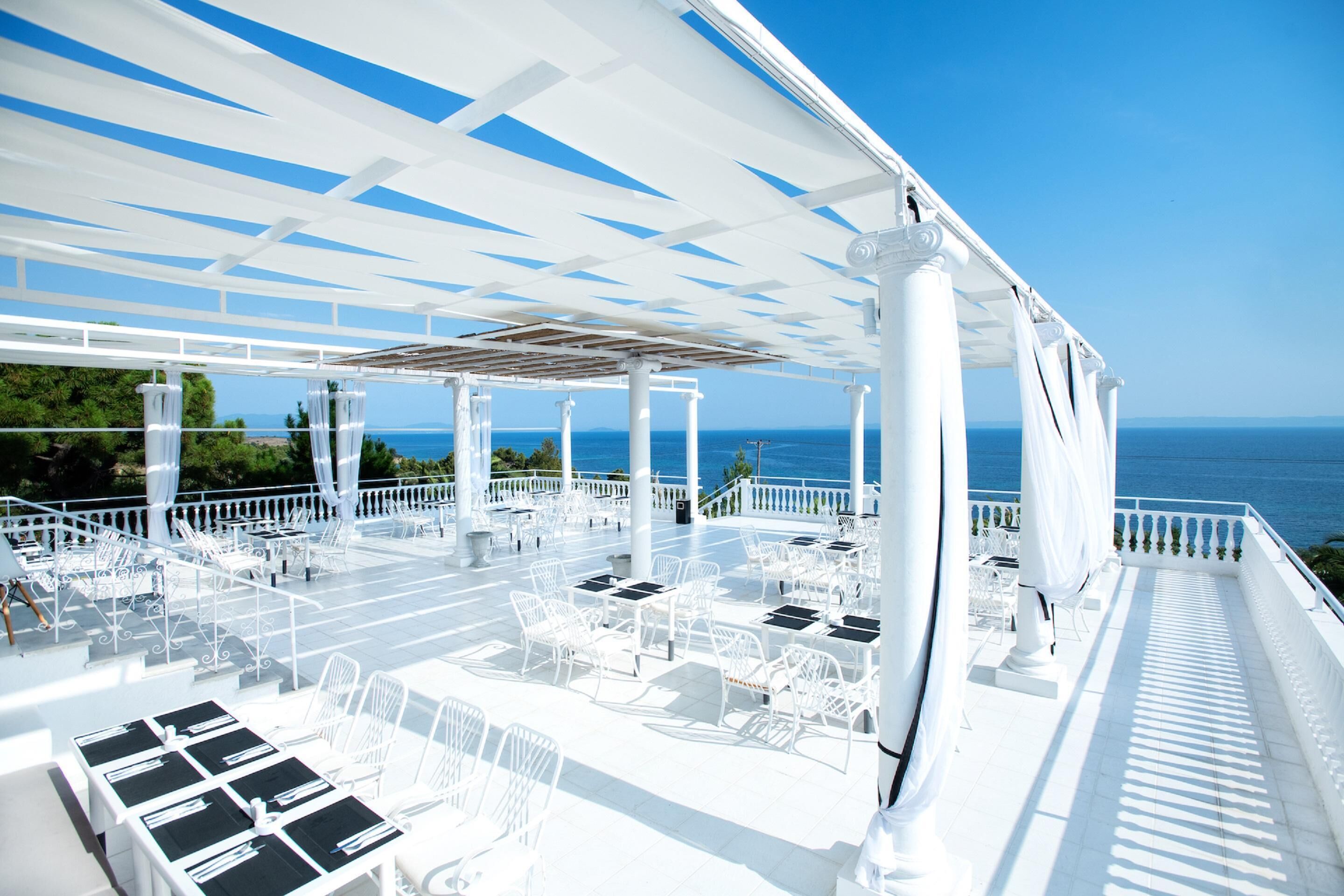 An outdoor terrace with white furniture and columns, overlooking the sea.
